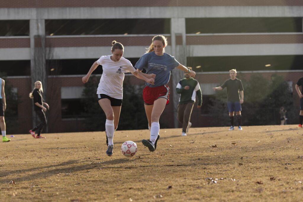Students playing soccer near a parking garage.